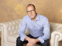 Christian Mentzel sitzt auf einem Sofa, und schaut selbstbestimmt authentisch, mit voller Stärke. Er stahlt innerer Ruhe und Selbstvertrauen aus.
